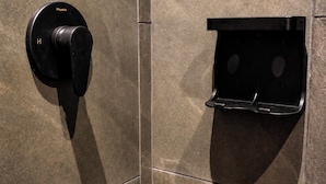 A bathroom with a black towel rack and a black towel dispenser mounted on a tiled wall.