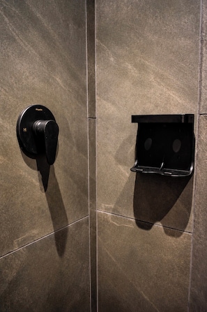 A bathroom with a black towel rack and a black towel dispenser mounted on a tiled wall.