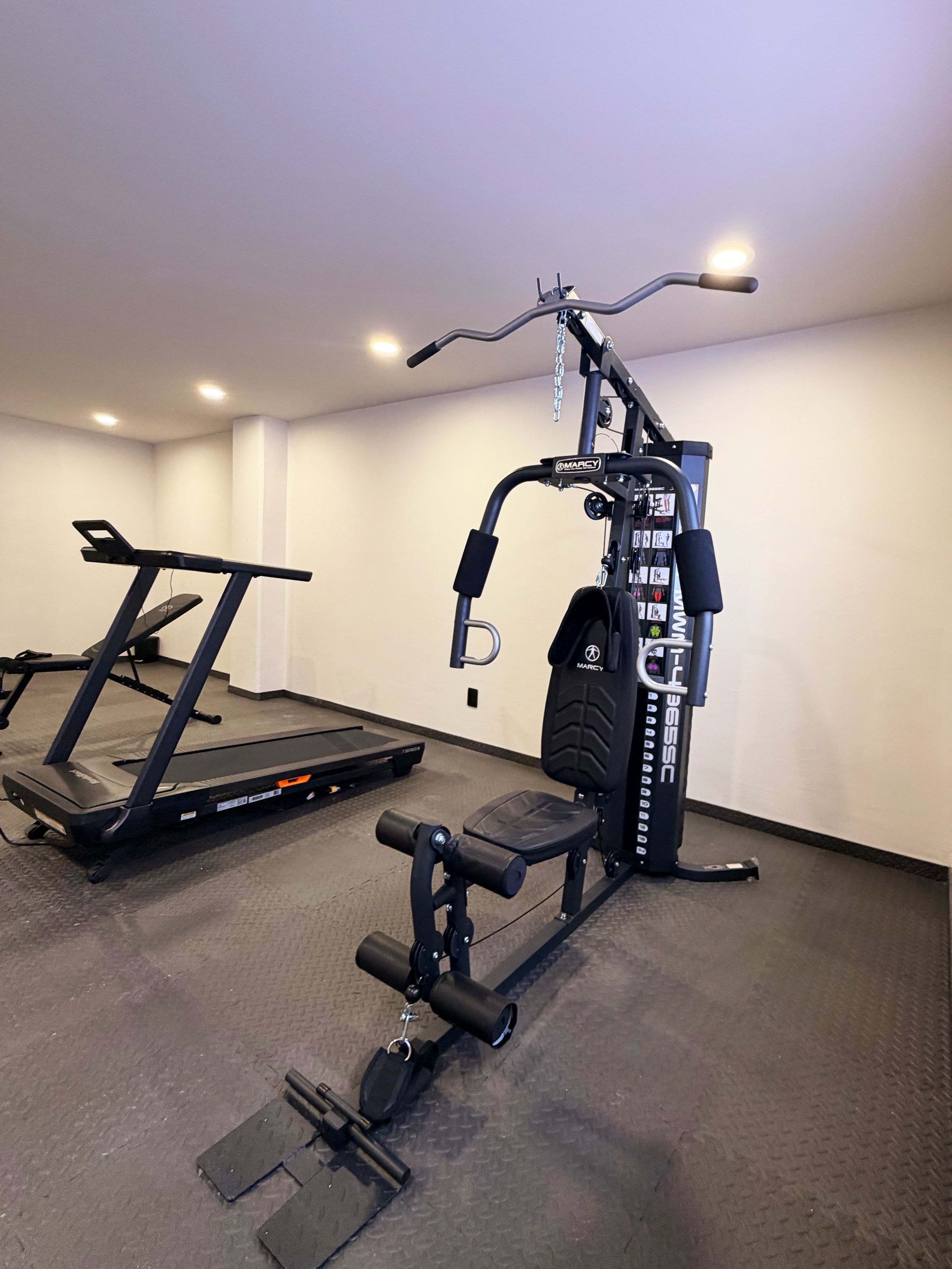 Un gimnasio con cinta de correr, banco de pesas y diversos equipos de ejercicio.