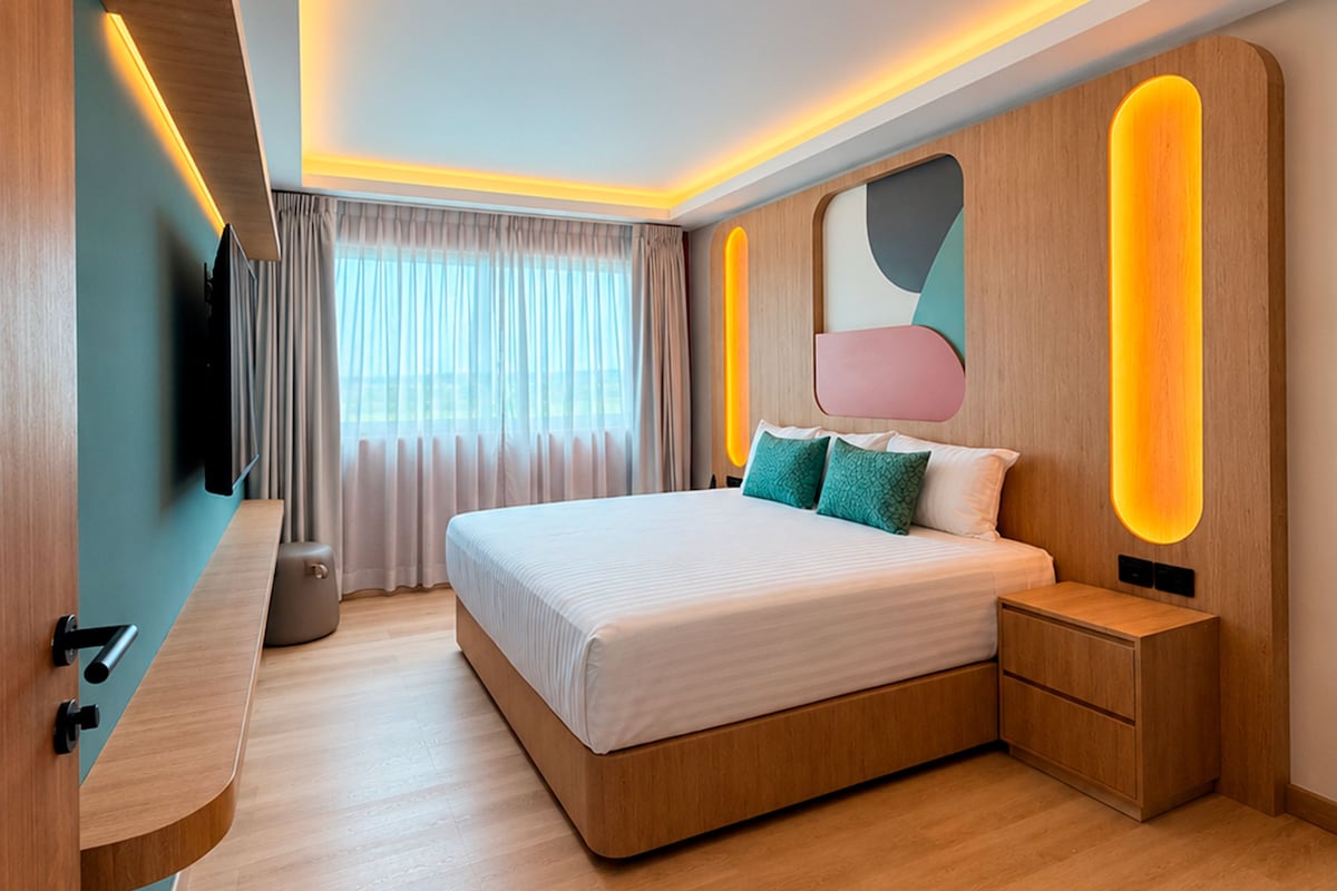 Quarto moderno com uma cama grande, mesas de cabeceira, televisão e janela com cortinas.