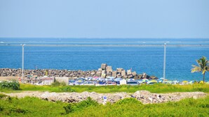 A coastal area with a rocky breakwater, parked cars, and beach umbrellas.