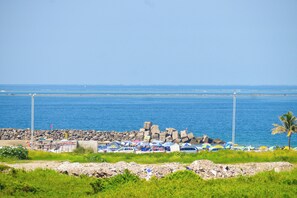 A coastal area with a rocky breakwater, parked cars, and beach umbrellas.