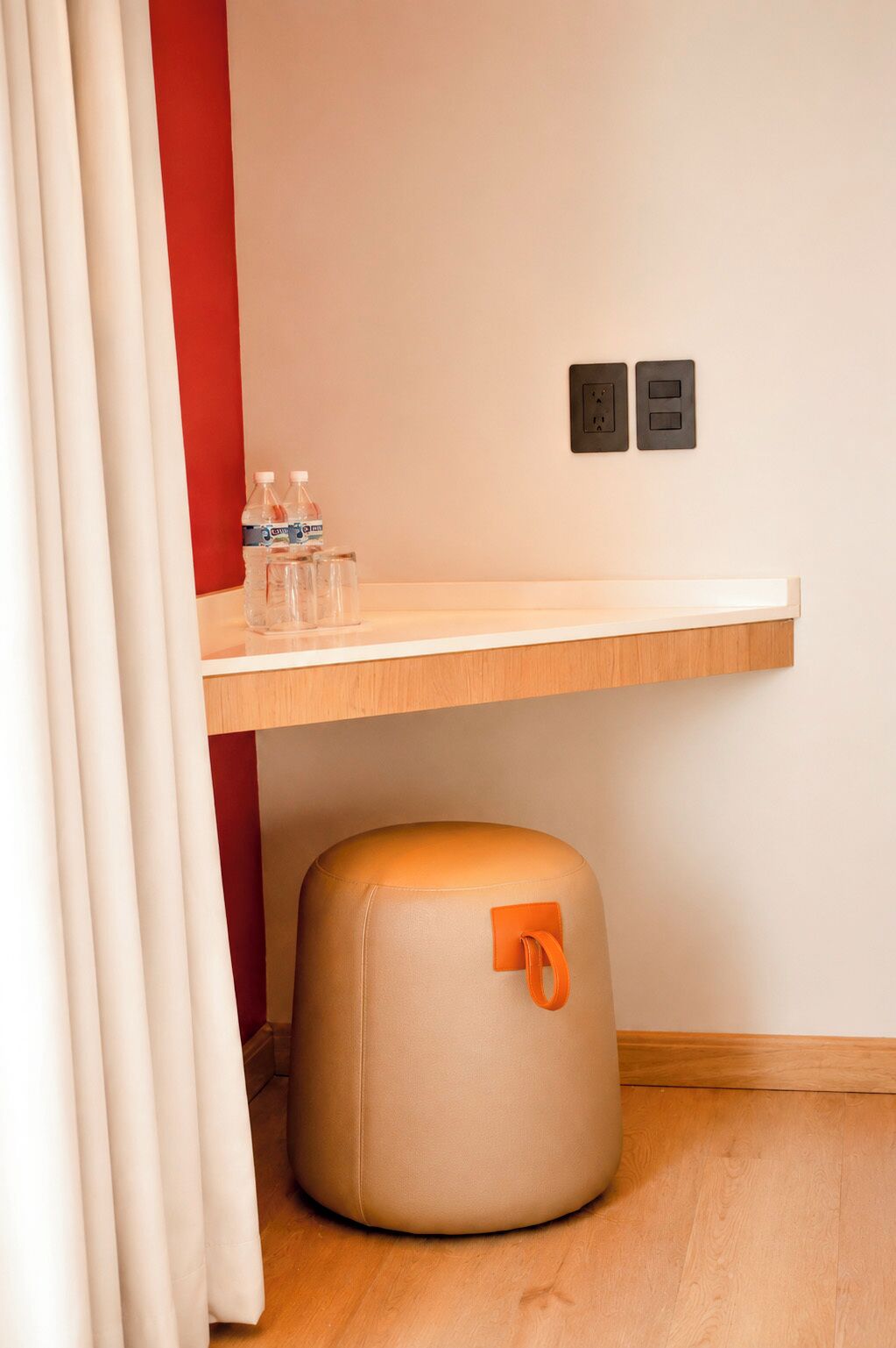 A room with a wooden shelf, a round ottoman, and a wall socket.