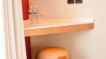 A room with a wooden shelf, a round ottoman, and a wall socket.