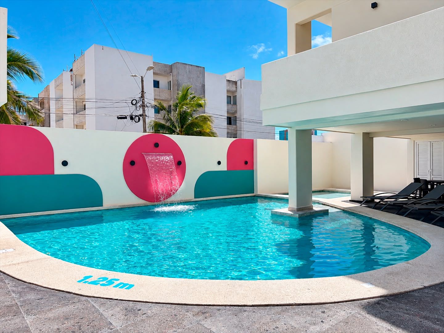 Une piscine avec un toboggan, entourée d’un bâtiment blanc dont les murs sont agrémentés d’éléments décoratifs colorés.