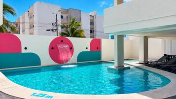 Une piscine avec un toboggan, entourée d’un bâtiment blanc dont les murs sont agrémentés d’éléments décoratifs colorés.