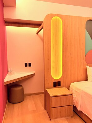 Um quarto moderno com cabeceira de madeira, mesa de cabeceira, pequeno aparador e cama com roupa de cama branca.