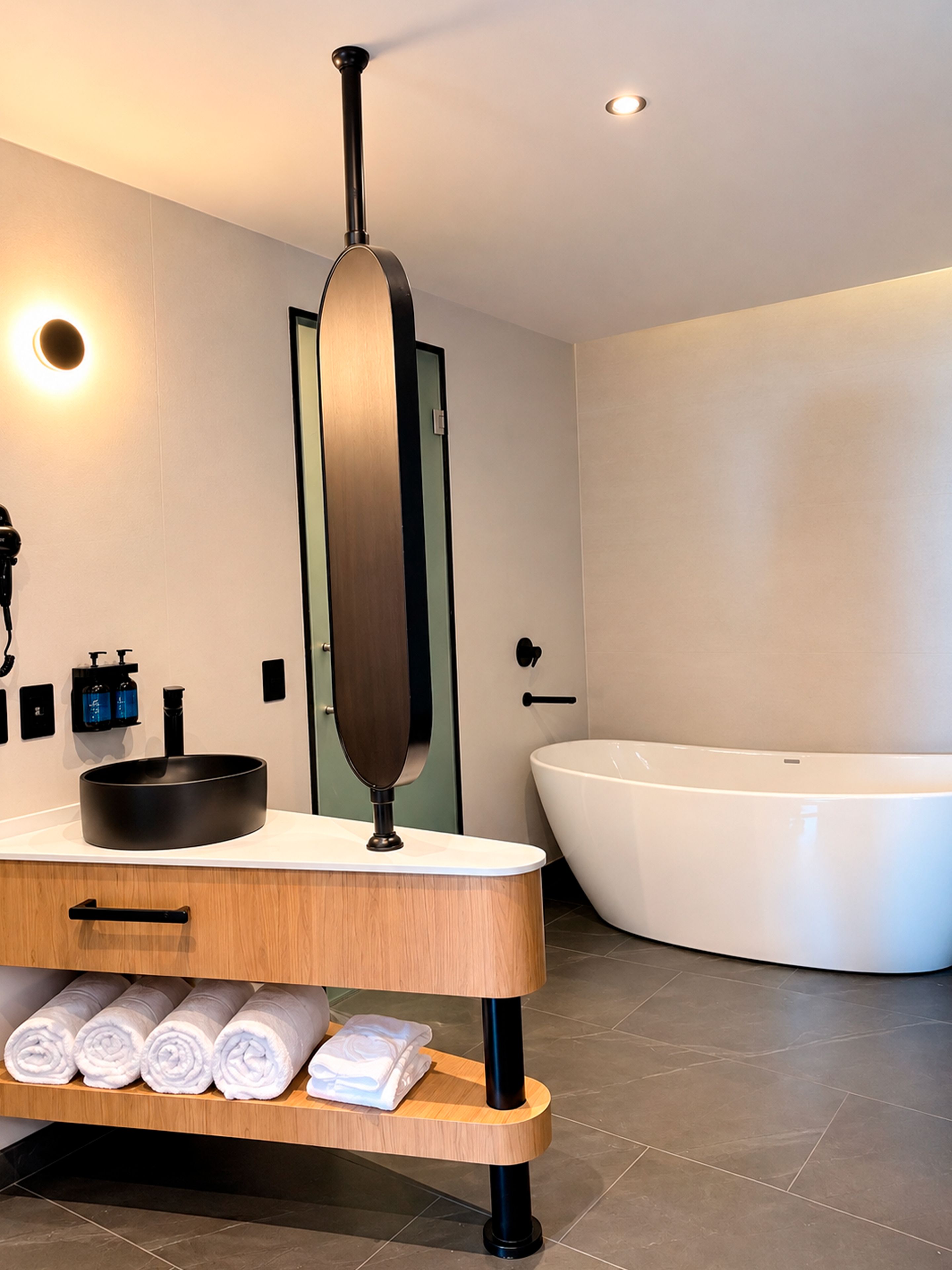 Un baño moderno con una bañera grande, un tocador de madera con lavamanos y un perchero para toallas.