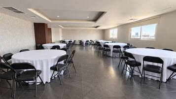 Un salón de conferencias con varias mesas redondas y sillas, ventanas amplias y un revestimiento de pared con diseño.