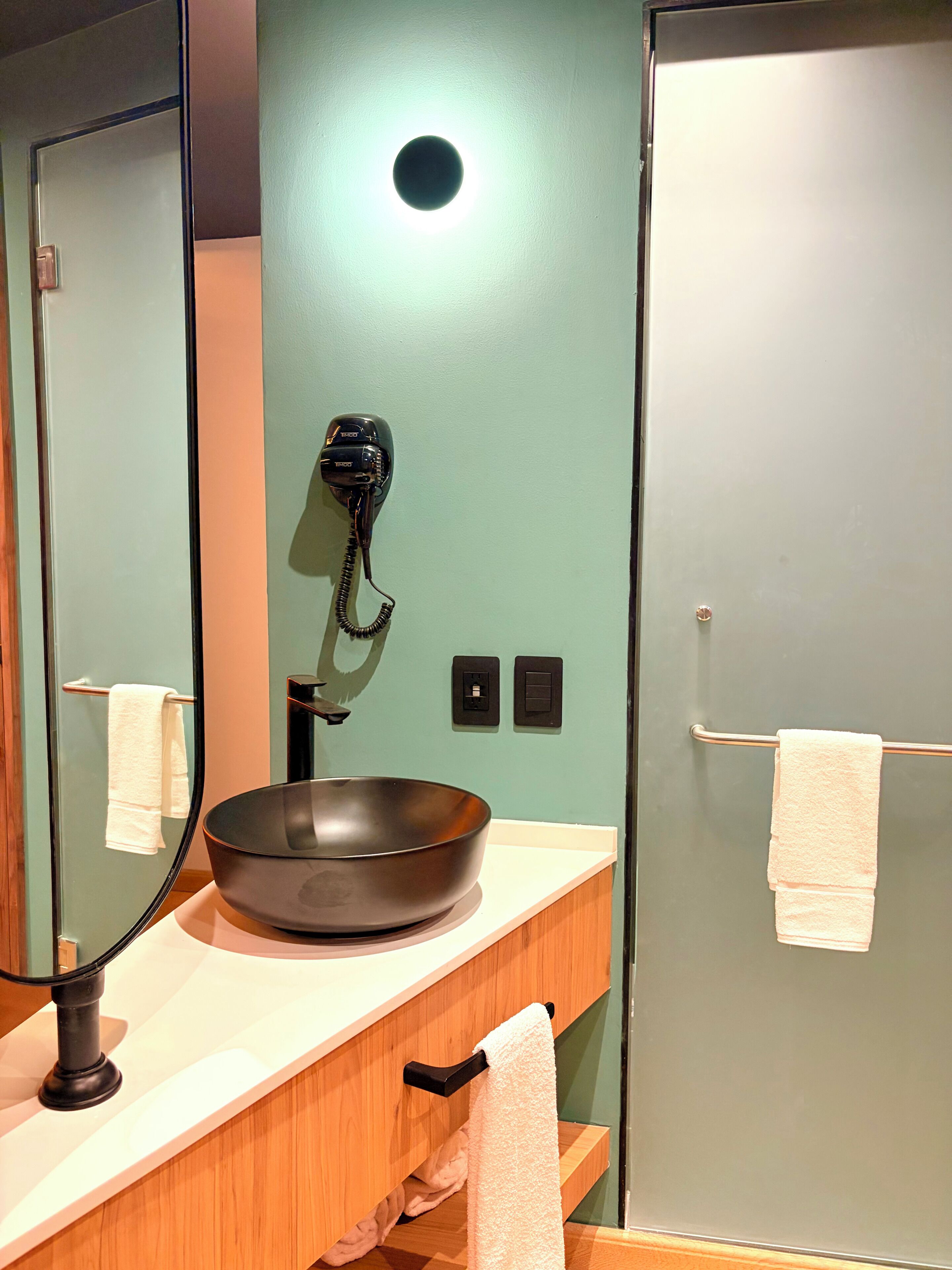 Une salle de bain avec un lavabo rond, un sèche-cheveux fixé au mur et un porte-serviettes.