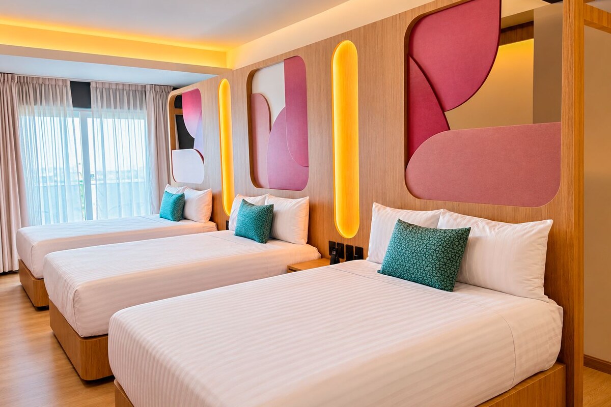 Quarto de hotel com três camas, uma janela grande com cortinas e um design moderno na parede com formas geométricas.