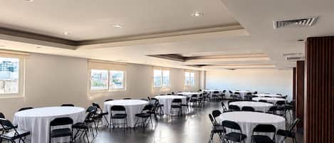 A conference room with multiple round tables and chairs, large windows, and a modern ceiling design.