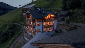 A multi-story wooden house with balconies, solar panels, and a view of a hilly landscape. - Vrbo Property (Marebbe)