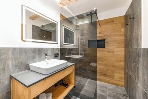 A modern bathroom with a large mirror, two sinks, and a shower area. - Vrbo Property (Marebbe)