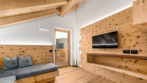 A modern interior with a wooden bench, a flat-screen TV mounted on a wooden wall, and a door leading to an outdoor area. - Stay calm! Family-Friendly Apartment in Val Badia: Experience the Dolomites (Marebbe)