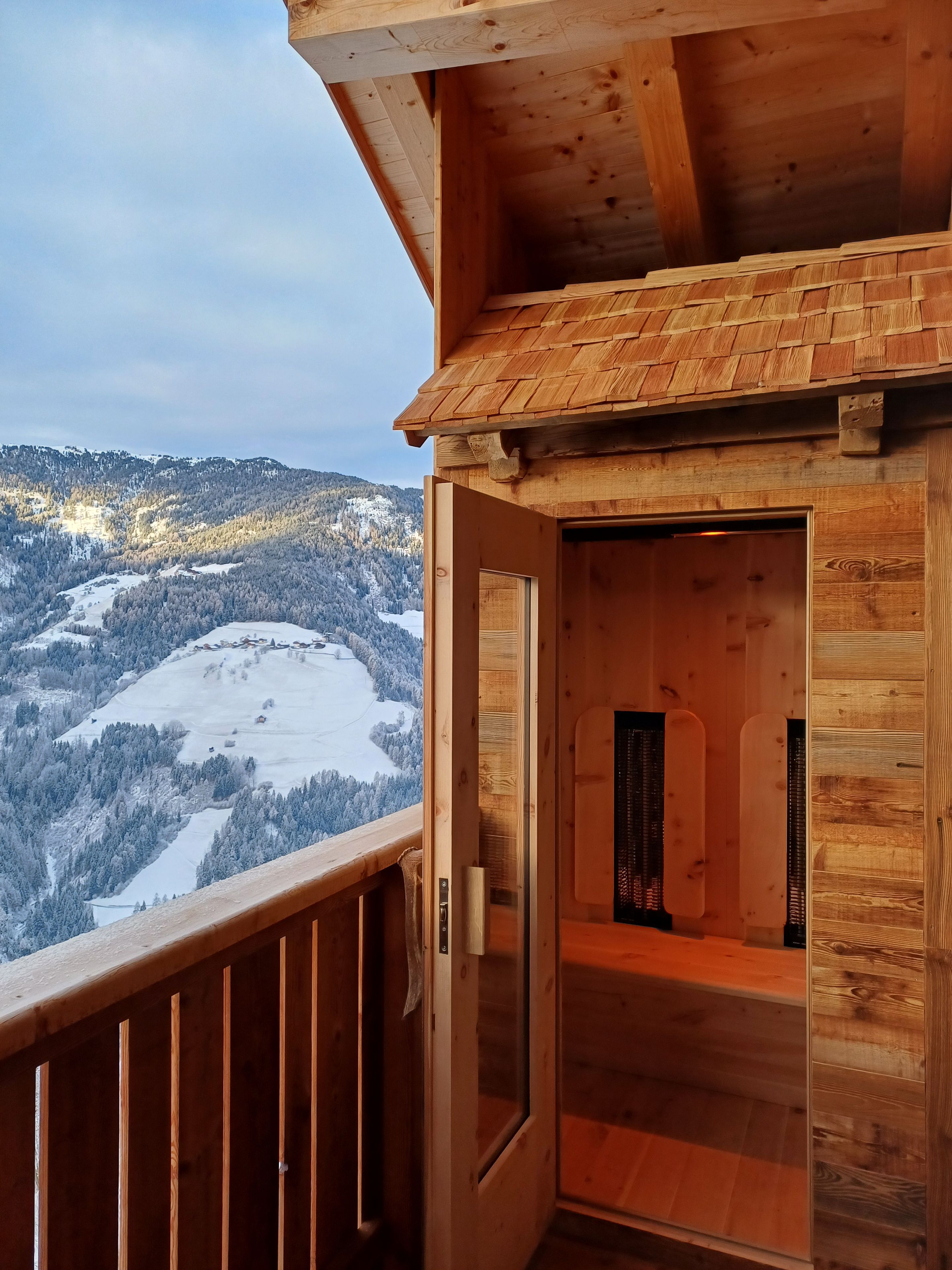 A wooden cabin with a balcony overlooking a snowy mountain landscape.