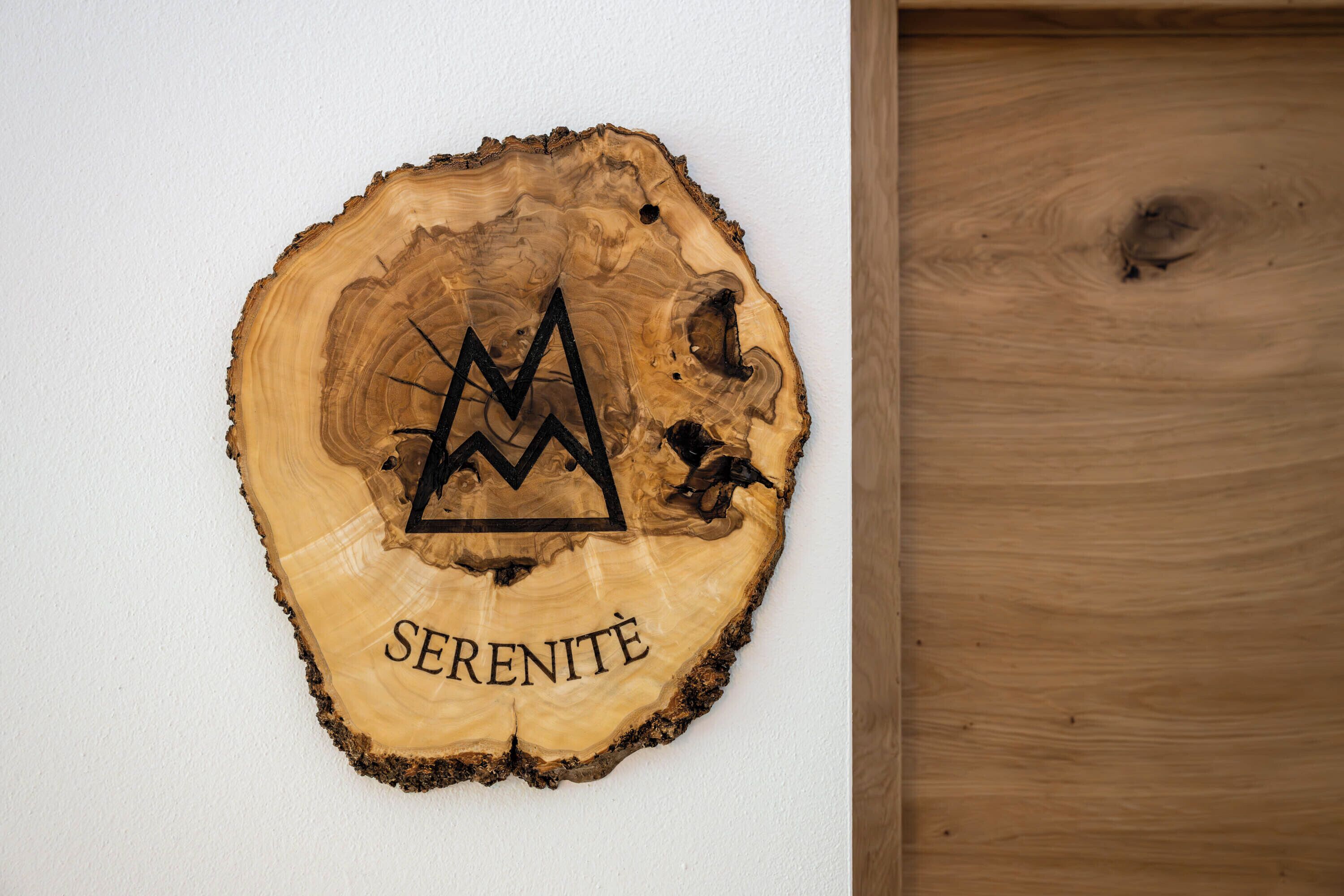 Una rebanada de madera con un diseño de cima de montaña y la palabra 'SERENITE' sobre una pared blanca.