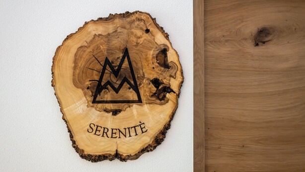 A wooden slice with a mountain peak design and the word 'SERENITE' on a white wall. - Vrbo Property (Marebbe)