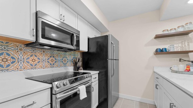 A modern kitchen with stainless steel appliances, a patterned backsplash, and a tiled floor. - The Fairway at the Pointe Royale (Branson)