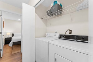 A laundry room with a white washing machine and dryer, a metal drying rack, and a wall-mounted heater. - The Fairway at the Pointe Royale (Branson)