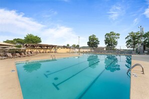A swimming pool with lounge chairs, a covered seating area, and trees in the background. - The Fairway at the Pointe Royale (Branson)