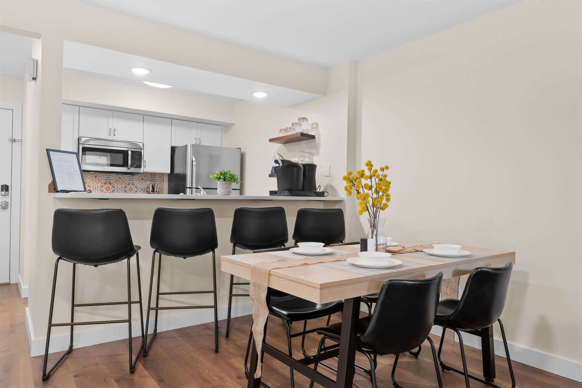 Une cuisine moderne avec un coin repas, comprenant une table avec des chaises et un vase rempli de fleurs jaunes.