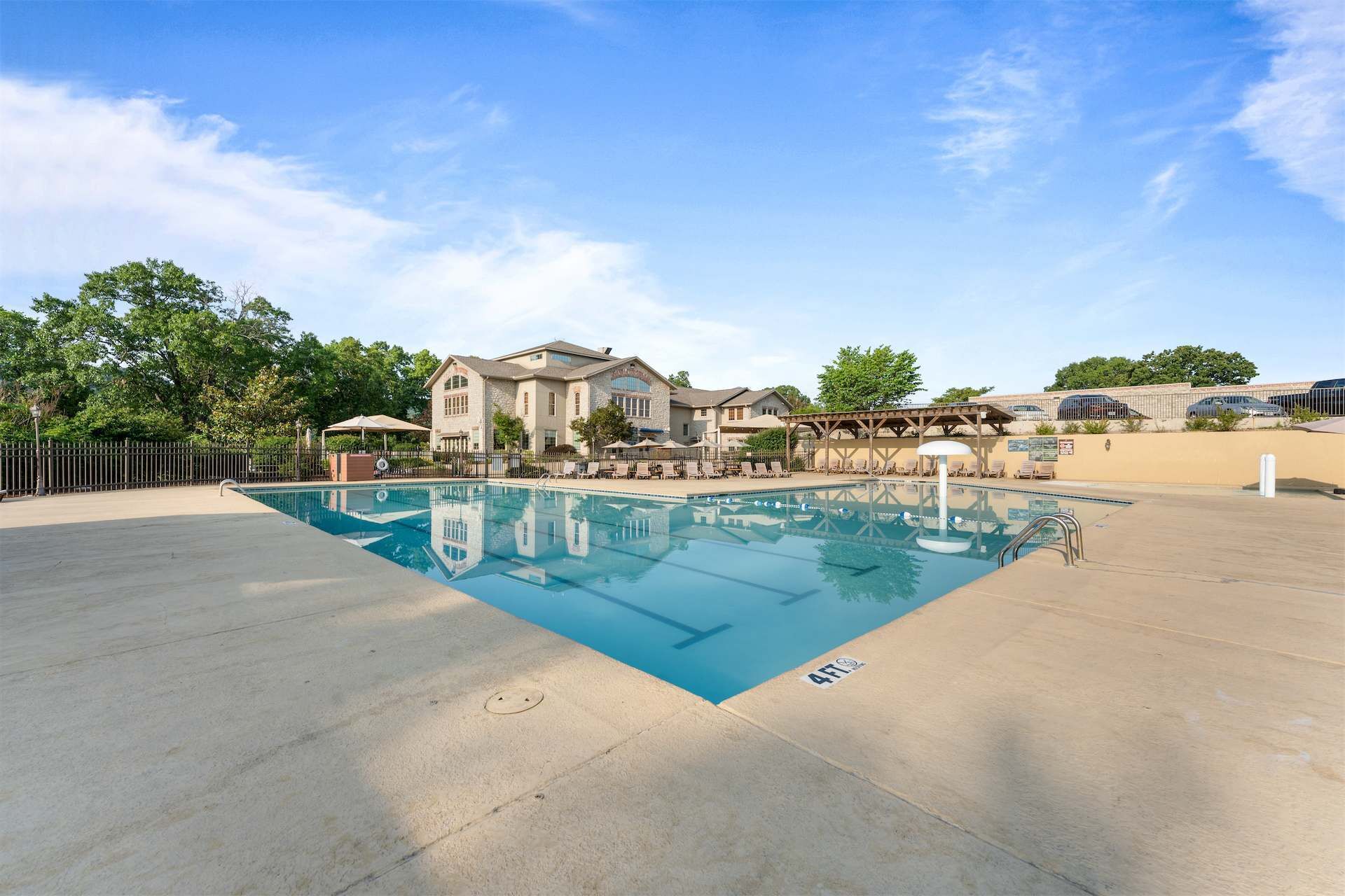 A swimming pool with a clear blue water, surrounded by a concrete deck, and a building with a stone facade in the background.