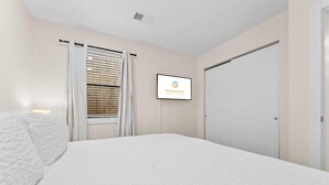 A hotel room with a bed, a window with blinds, a wall-mounted TV displaying 'GRAND WELCOME,' and a door. - The Fairway at the Pointe Royale (Branson)