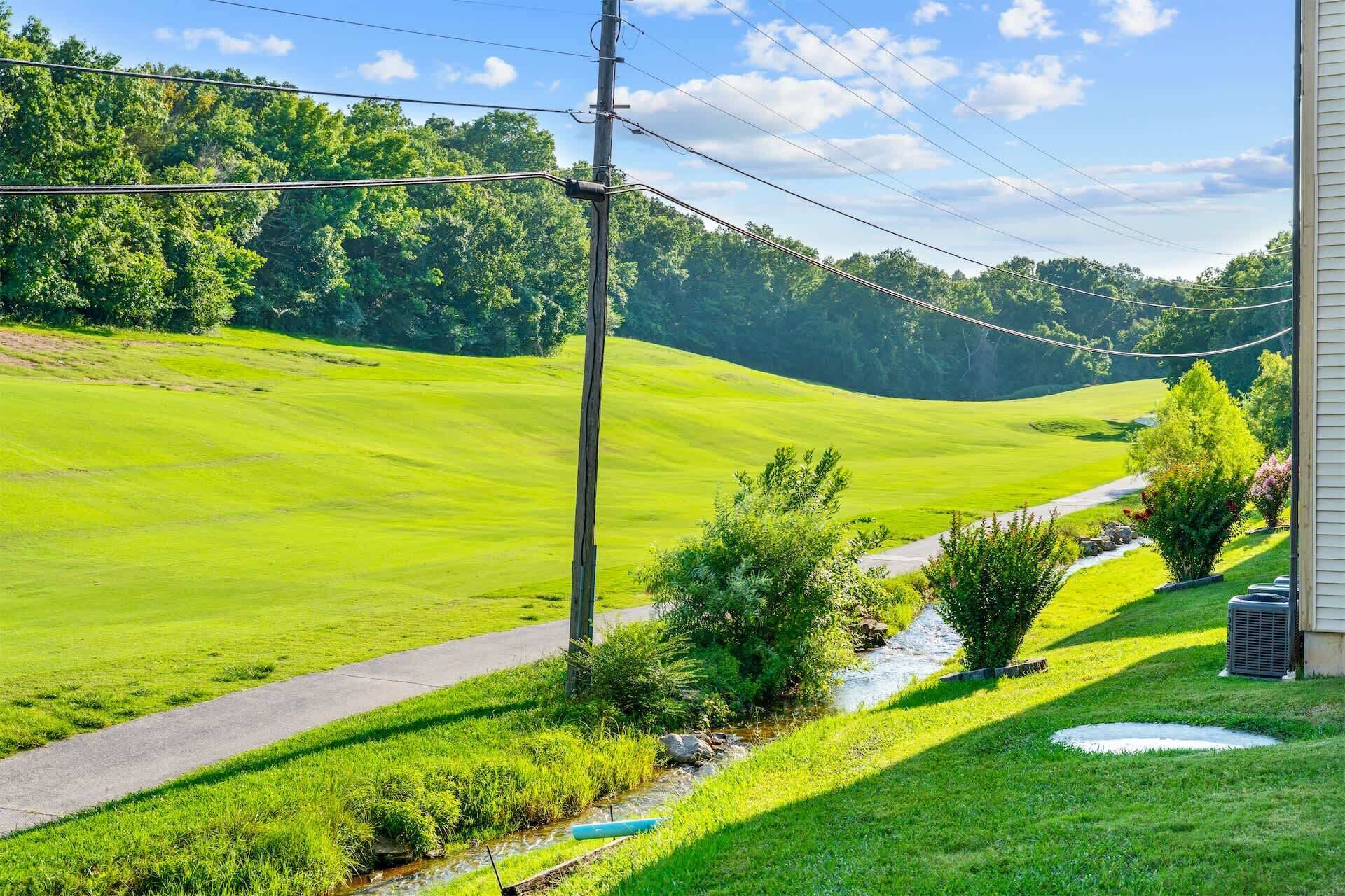 A residential property with a paved driveway, a small stream, and lush greenery.