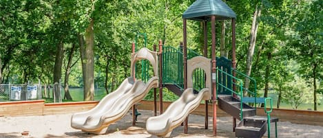 A playground with two slides, a climbing structure, and a small shelter.