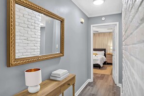 A hallway with a mirror, a bedside table with books, and a bed in the adjacent room. - Dalraida 3BR Near Gunter Annex & Downtown (Montgomery)