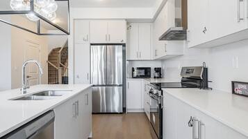 A modern kitchen with stainless steel appliances, white cabinetry, and a wooden floor.