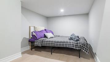 Une petite chambre avec un lit simple, une couvre-lit à carreaux, un oreiller blanc et une couverture violette.