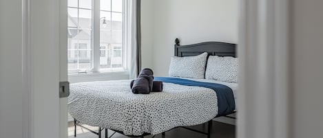 A bedroom with a bed, a window, and a view of buildings outside.