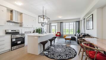 A modern kitchen with a central island, a dining area with a round table, and a living space with a sofa and a red chair.