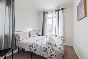 Ein Schlafzimmer mit einem Bett, einem Sessel, einem Fenster mit Vorhängen und einem Wandbild.
