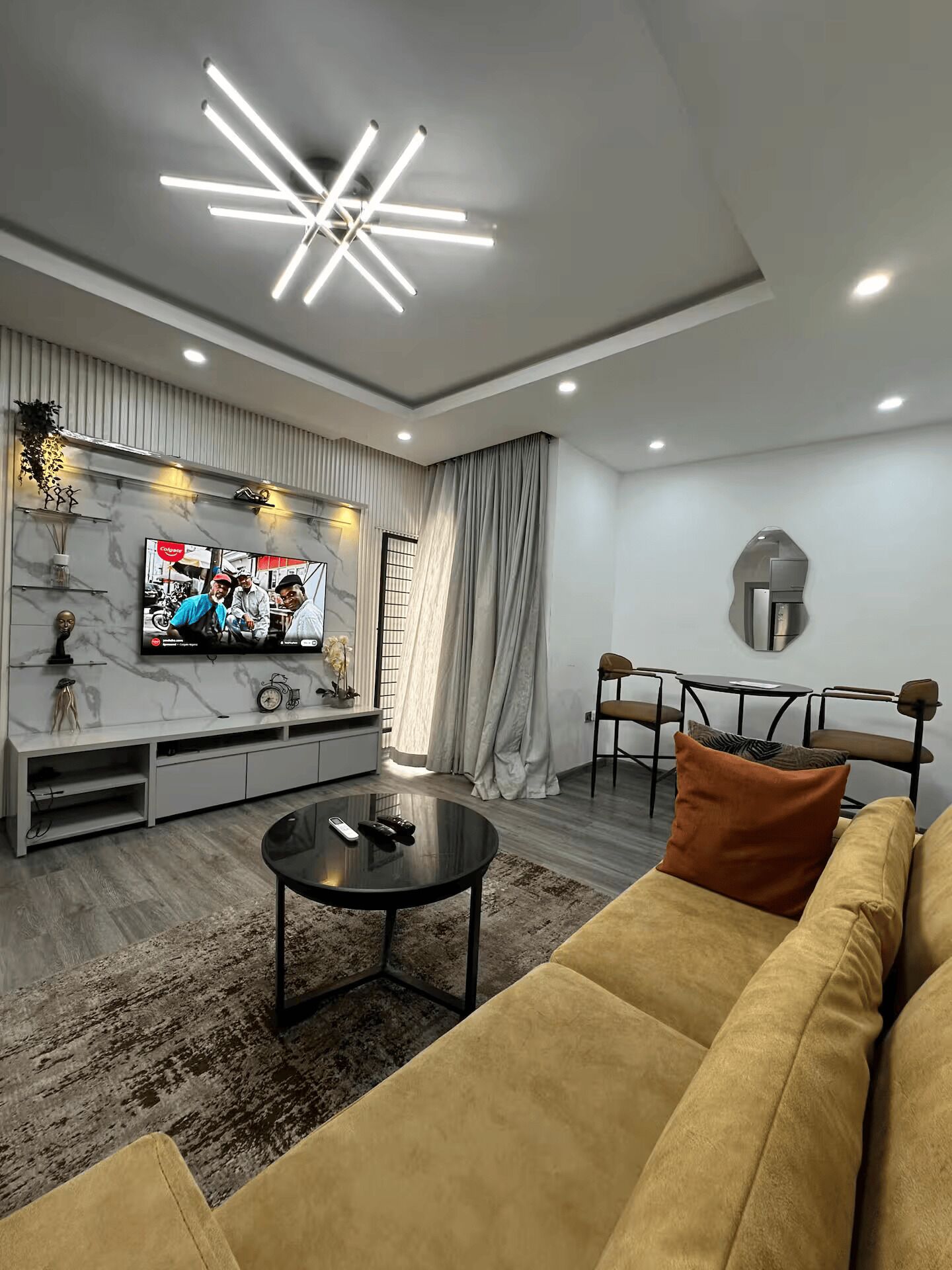 A modern living room with a flat-screen TV, a sofa, a coffee table, and a dining area with chairs.