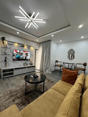 A modern living room with a flat-screen TV, a sofa, a coffee table, and a dining area with chairs. - Premium 1-Bedroom Apartment in Lekki 1 with Fast Wi-Fi & 24/7 Power (Lekki)
