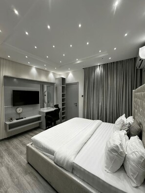 A modern bedroom with a large bed, a TV mounted on the wall, a desk with a chair, and a wardrobe. - Premium 1-Bedroom Apartment in Lekki 1 with Fast Wi-Fi & 24/7 Power (Lekki)