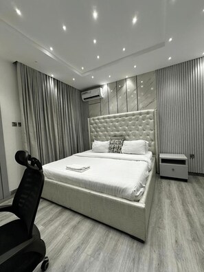 A modern bedroom with a large bed, a bedside table, an air conditioning unit, and a chair. - Premium 1-Bedroom Apartment in Lekki 1 with Fast Wi-Fi & 24/7 Power (Lekki)