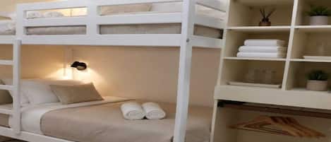 Una cama individual sobre otra con una estantería al lado, donde hay toallas dobladas y una planta en maceta.