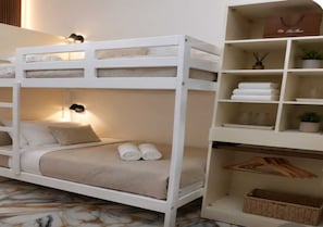 Uma cama beliche com uma estante ao lado, contendo toalhas dobradas e um vaso de planta.
