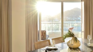 Ein Essbereich mit Tisch für zwei Personen, einer Blumenvase und Blick auf einen Berg durch große Fenster.