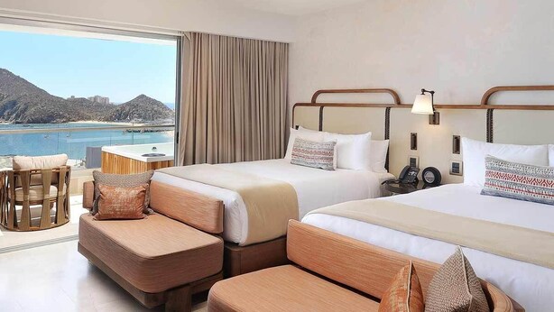 Ein Hotelzimmer mit zwei Betten, einem Schlafsofa, einem kleinen Tisch und Meerblick.