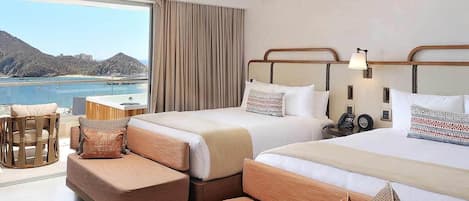 Habitación de hotel con dos camas, un sofá, una mesita y vista al mar.