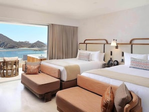 Ein Hotelzimmer mit zwei Betten, einem Schlafsofa, einem kleinen Tisch und Meerblick.