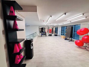 A spacious lobby with a modern design, featuring a black and pink cone display, a coffee machine, and red chairs. - Apartment, 2BR/2BA, AC and Heating, parking y GYM. (Ñuñoa)