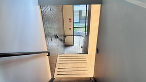 En moderne trappe med gelænder i metal, der fører til et udendørs område med en glasdør og en brandalarm.