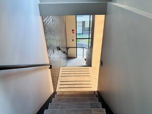 Eine moderne Treppe mit Metallgeländer, die zu einem Außenbereich mit Glastür und Rauchmelder führt.