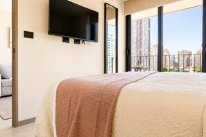 A bedroom with a large bed, a flat-screen TV mounted on the wall, and a balcony with a view of high-rise buildings. - Apartment, 2BR/2BA, AC and Heating, parking y GYM. (Ñuñoa)